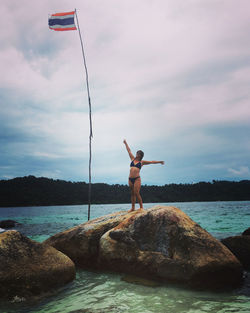 Rear view of woman doing yoga on rock by sea against sky
