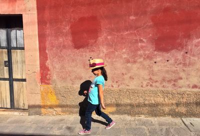 Side view of girl walking on sidewalk by building