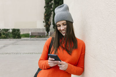 Young woman using mobile phone while standing on wall
