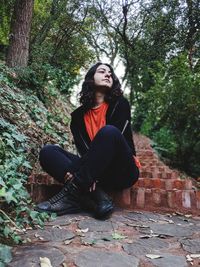 Young woman looking away while sitting on tree in forest