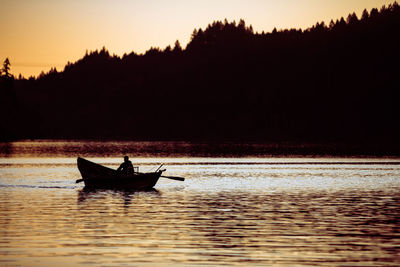 Silhouette man in boat on lake against sky during sunset