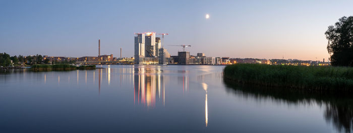 Illuminated buildings by river against sky