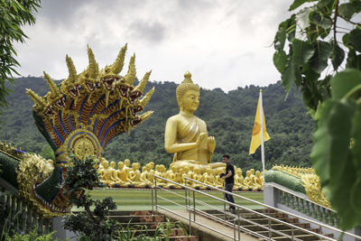 Man standing by railing against buddha statue and sky