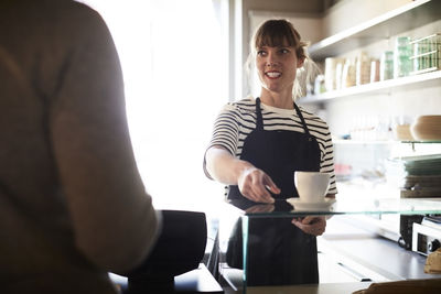 Smiling female barista serving coffee to male customer at cafe