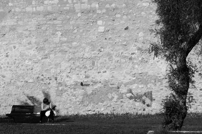 Woman sitting on bench against stone wall