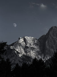 Low angle view of moon in mountains against sky