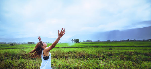 Rear view of woman with arms raised standing on field against sky