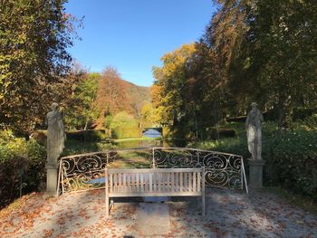 Empty bench by trees against sky during autumn