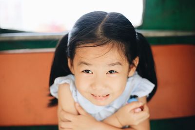 Close-up portrait of girl with arms crossed making face while sitting by window at home