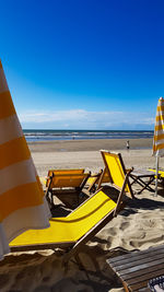 Yellow deck chairs on beach against blue sky