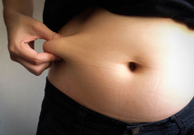 Midsection of overweight woman holding stomach fats while standing against wall