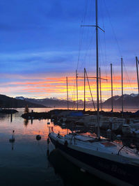 Boats moored in harbor at sunset