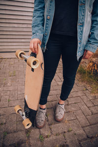 Low section of man holding skateboard while standing on footpath