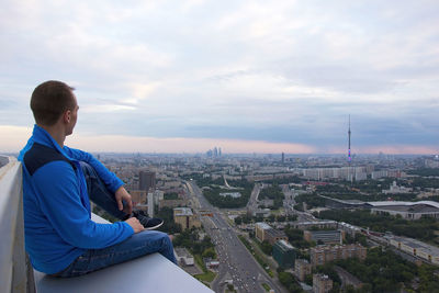 Rear view of man sitting against buildings in city against sky