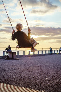 Woman sitting on swing at promenade against sky during sunset