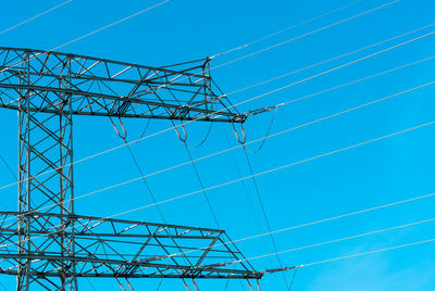 Low angle view of electricity pylon against blue sky