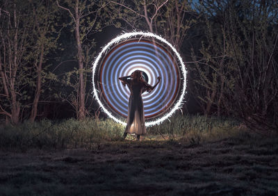 Woman standing against illuminated firework on field at night