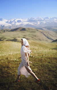 Beautiful woman with headscarf walking on grass against clear blue sky