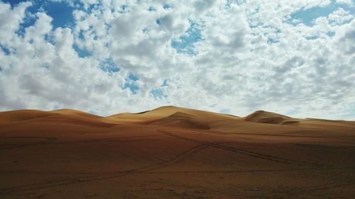 View of sand dunes in desert against cloudy sky