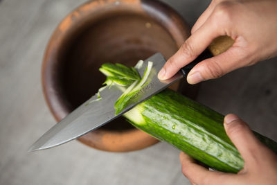 Cropped image of woman cutting cucumber over mortar and pastel