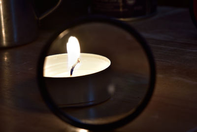 Close-up of lit tea light candle reflecting on mirror