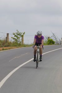 Woman riding bicycle on road against sky