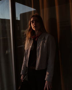 Young woman looking away while standing against window