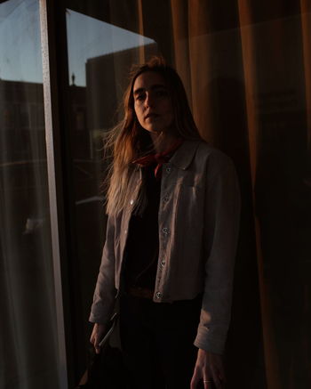 Portrait of young woman standing by window at home