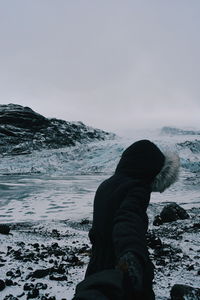 Man standing on rock by sea against sky during winter