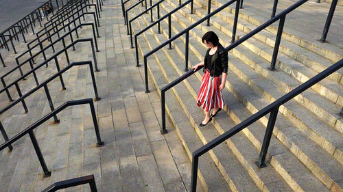 Full length of woman wearing striped skirt and jacket on steps amidst railing in city