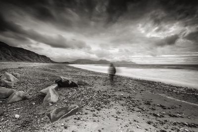 Blurred motion of person at beach by sea against dramatic sky