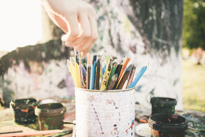 Cropped hand of person picking colored pencil from container