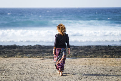 Rear view of woman walking at beach during sunny day