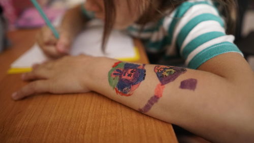 Midsection of girl with drawing on arm at table