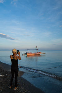 Rear view of woman standing at beach against sky