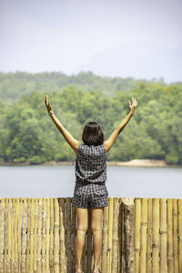 Rear view of woman with arms raised standing against lake