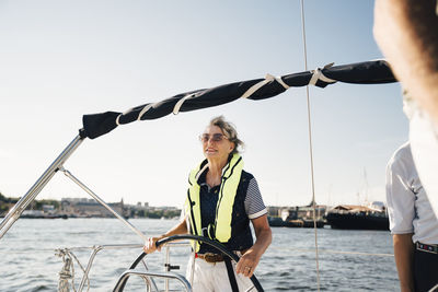 Active senior woman sailing boat with friends against clear sky on sunny day
