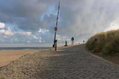 Cyclist on a paved path facing the sea in front of an empty beach at dawn