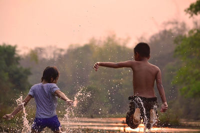 Children playing in river against sky at dusk