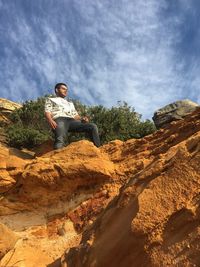 Man sitting on rock against sky