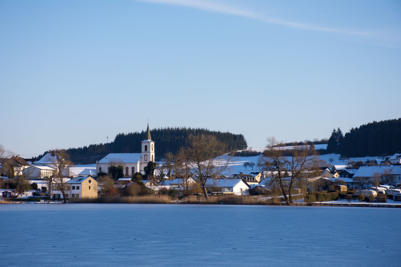 HOUSES BY FROZEN LAKE AGAINST CLEAR BLUE SKY