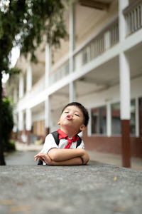 Portrait of cute boy sitting by school building