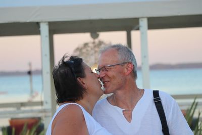 Smiling man kissing woman against sea