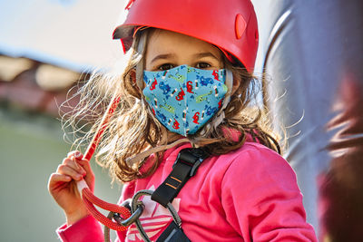 Little girl with protections practicing climbing between trees with ropes and nets