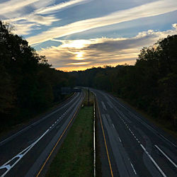 Highway amidst trees against sky during sunset