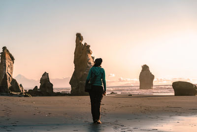 People standing on rock at beach against sky during sunset