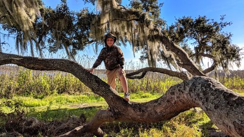 Portrait of boy standing on tree trunk against sky