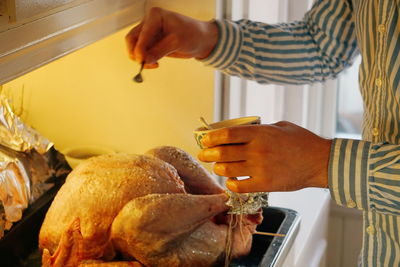 Midsection of woman seasoning roasted meat at kitchen