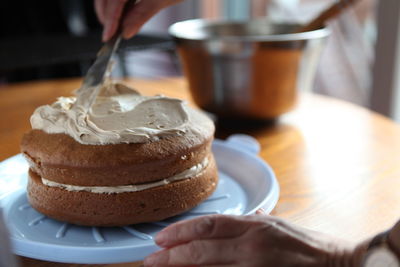 Cropped hand spreading cream on cake