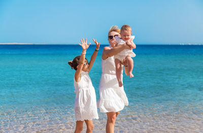 Friends with arms raised standing at beach against sky